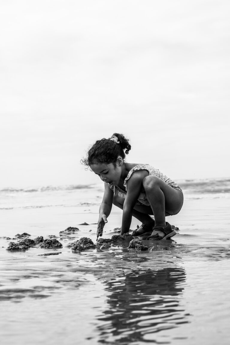 Photo en noir et blanc d'une petite fille jouant avec le sable au bord de la mer