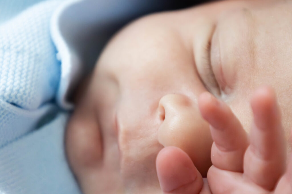 Séance photo - naissance. Un bébé endormi dans son pyjama bleu en gros plan, une main sur les yeux